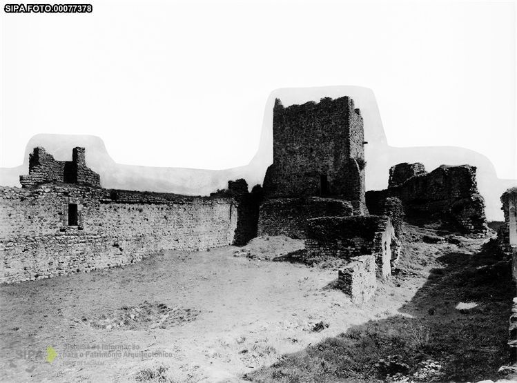 Interior do Castelo de Pombal visto do pátio, com a torre de menagem e os panos de muralha em ruínas, em fotografia de arquivo a preto e branco.